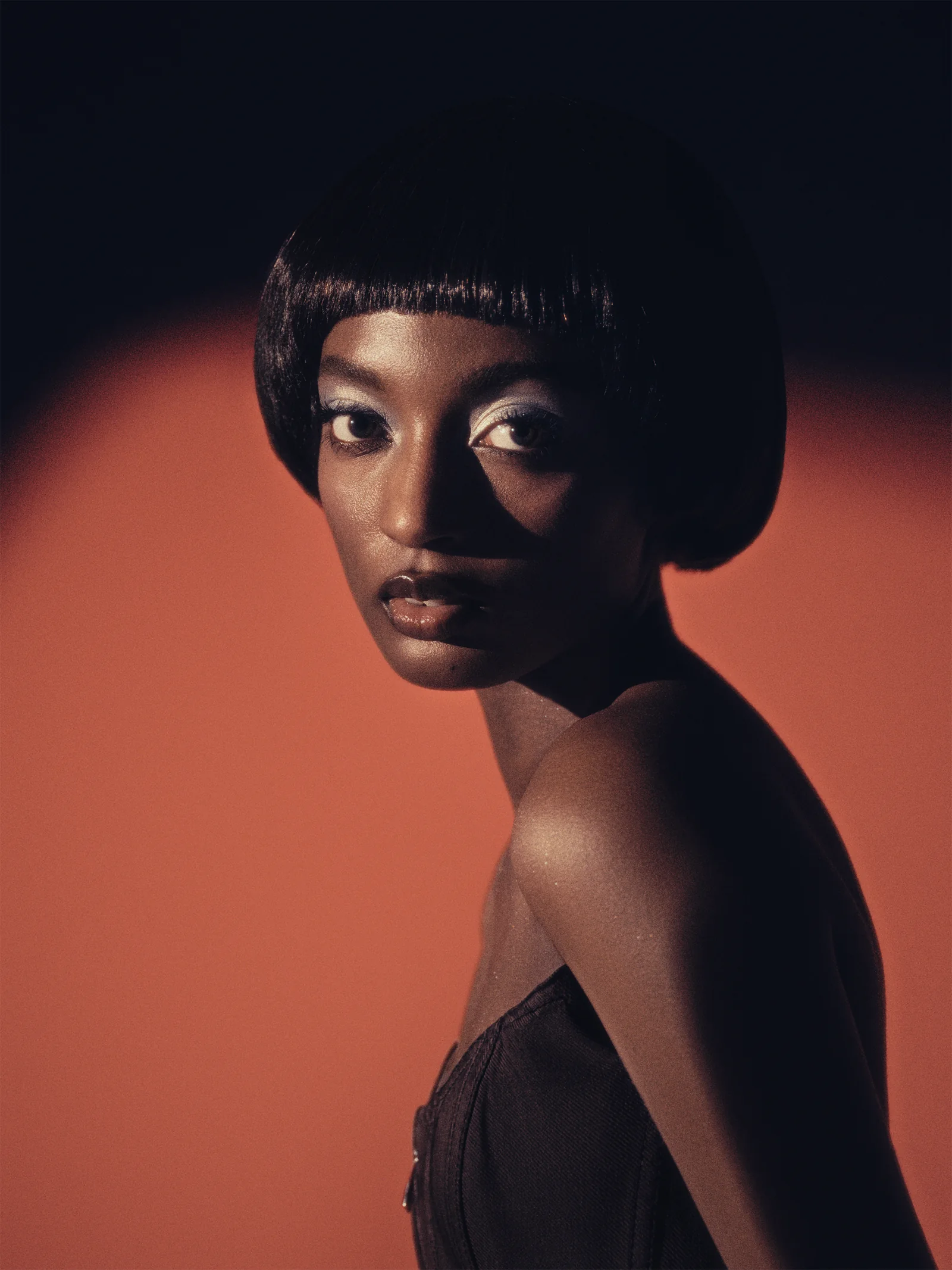 Portrait with a sharp dark bob, hard light across the face, against a terracotta field